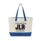 An off-white canvas tote bag with royal blue handles and bottom trim, featuring a front pocket with a black 'JLR INVESTIGATES' logo print, set against a plain white background.