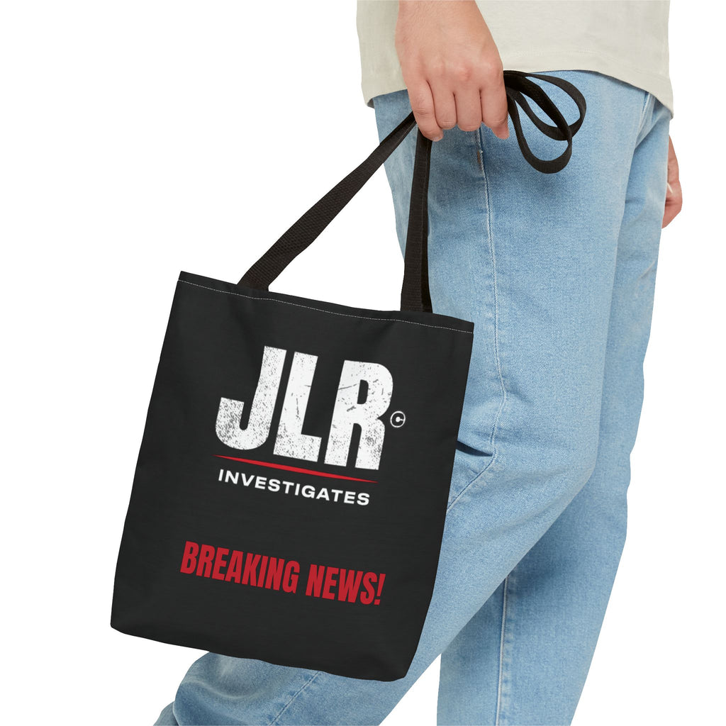 Lifestyle image of a person carrying a black JLR© Investigates tote bag with a white logo and red “BREAKING NEWS!” graphic.