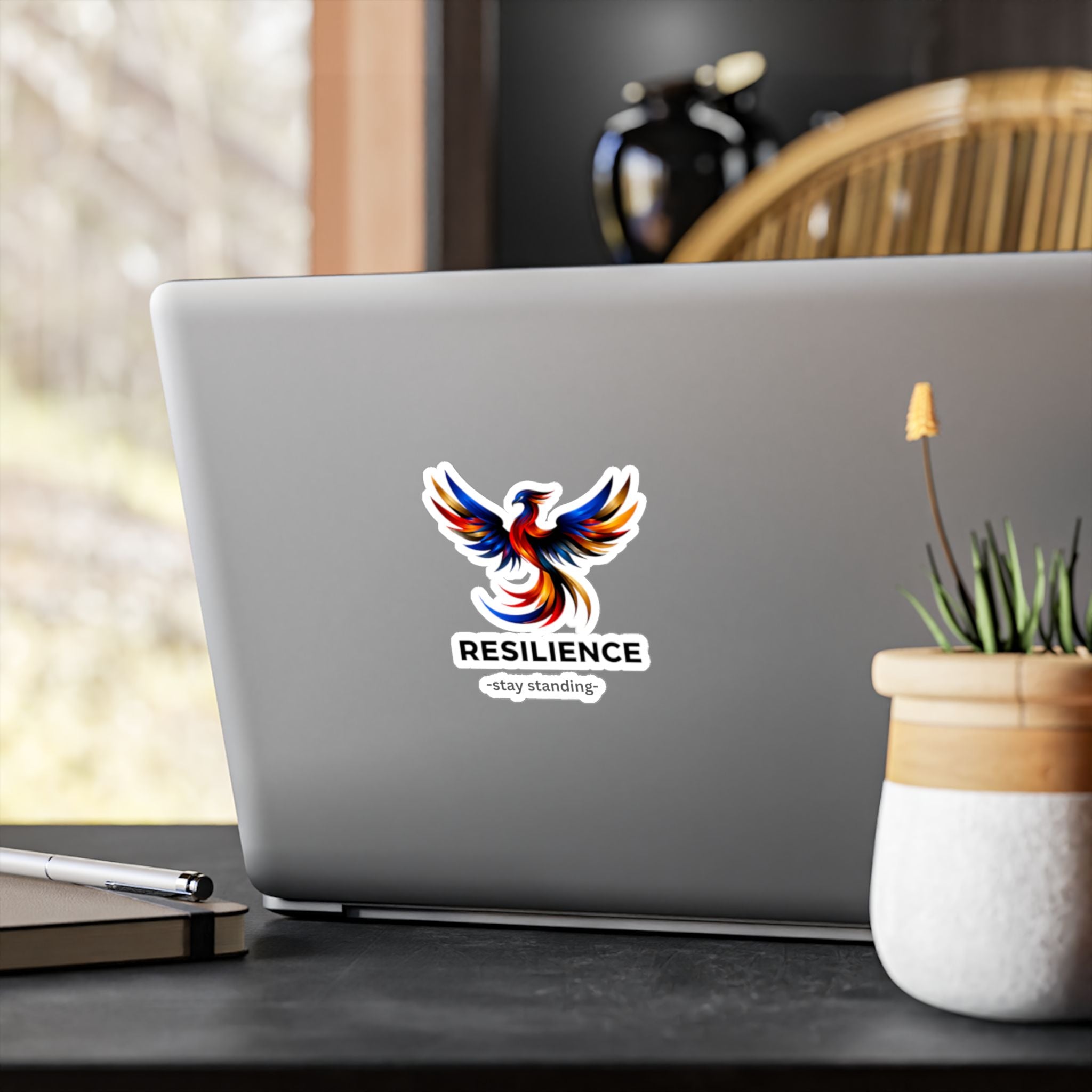 Resilience phoenix sticker displayed on a surface next to a white cup