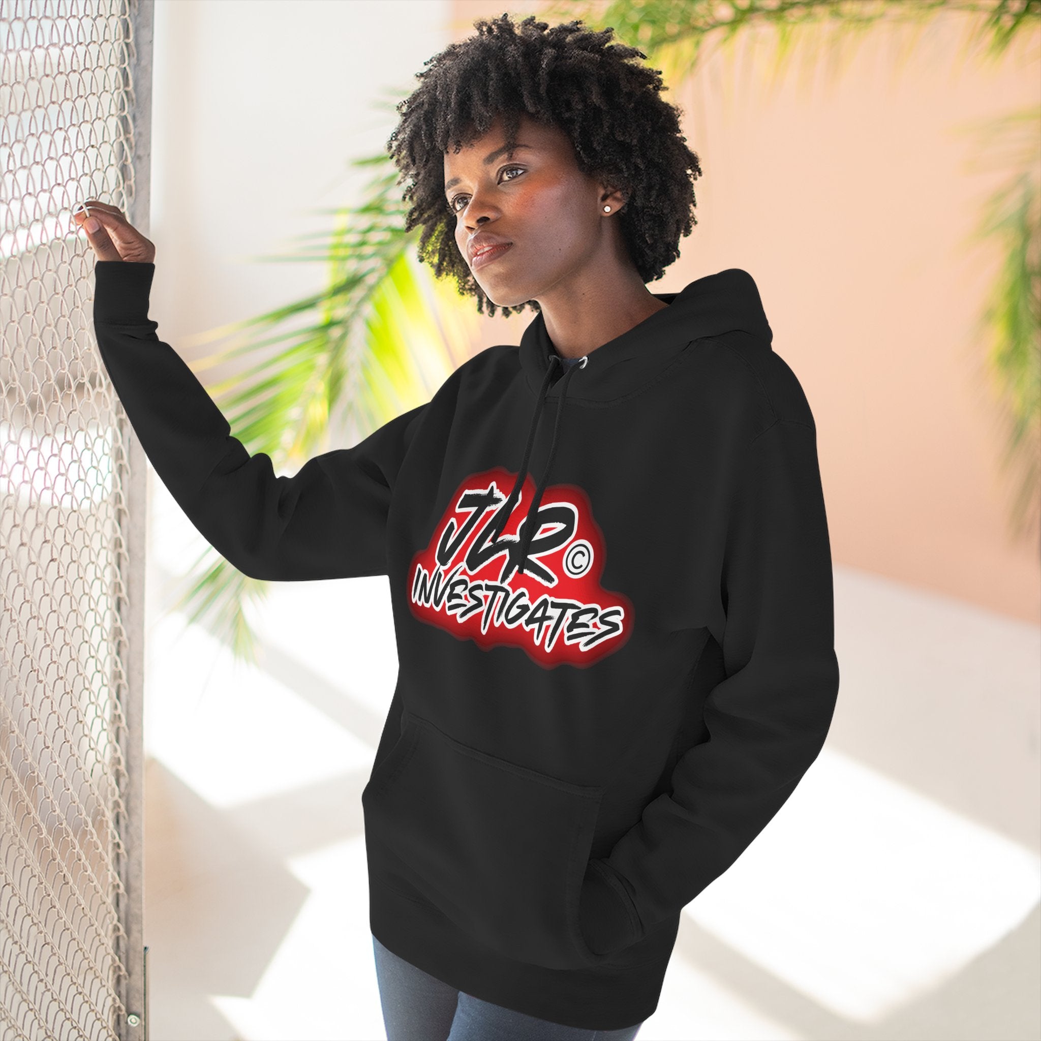 Woman wearing JLR© Bold Logo Hoodie in Black — graffiti-style JLR Investigates graphic on a pullover hoodie with kangaroo pocket and adjustable drawstring hood