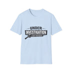 Light blue unisex t-shirt featuring a bold 'Under Investigation — JLR© Investigates' graphic with a magnifying glass icon and black and white banner design