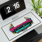 A large white desk mat with a colorful 'Whimpoole Wednesday!' graphic sits on a white desk in front of a computer monitor and keyboard. The desk mat has a black border and the brand name 'JLR©' printed in the lower right of the design.