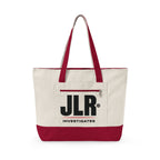 An off-white canvas tote bag with a dark red bottom panel and matching dark red handles, featuring a front pocket with a black 'JLR INVESTIGATES' logo, on a white background.