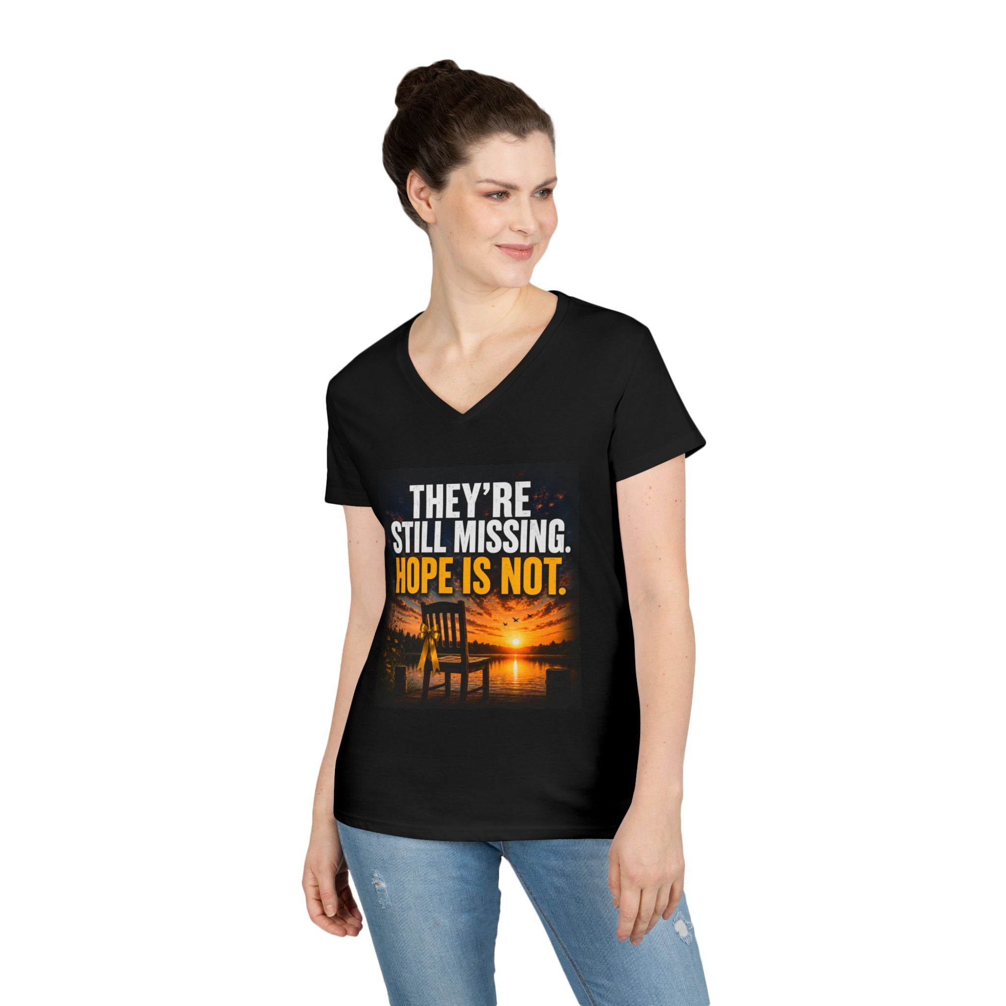 A woman modeling a black V-neck t-shirt with a graphic print that reads 'THEY'RE STILL MISSING. HOPE IS NOT.