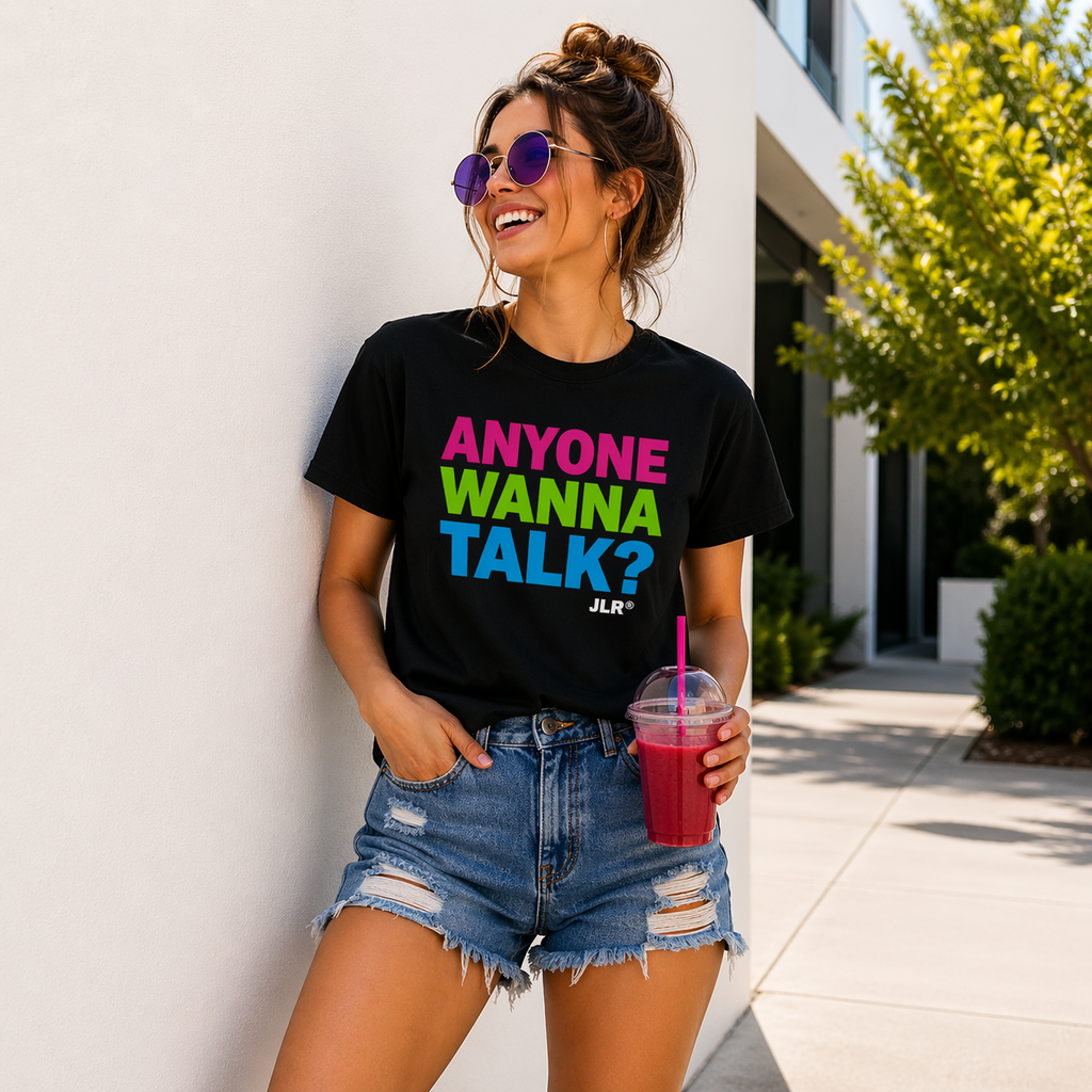 "Black unisex t-shirt with bold multicolor text reading 'Anyone Wanna Talk?' worn by a woman in sunglasses holding a drink — JLR Investigates apparel"