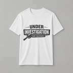 White unisex t-shirt featuring a bold 'Under Investigation — JLR© Investigates' graphic with a magnifying glass icon and black and white banner design