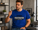 Man holding magnifying glass wearing blue unisex t-shirt featuring a bold 'Under Investigation — JLR© Investigates' graphic with a magnifying glass icon and black and white banner design