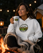 woman drinking coffee by campfire wearing White premium hoodie featuring the JLR© Army circular badge graphic with diverse illustrated figures on the chest