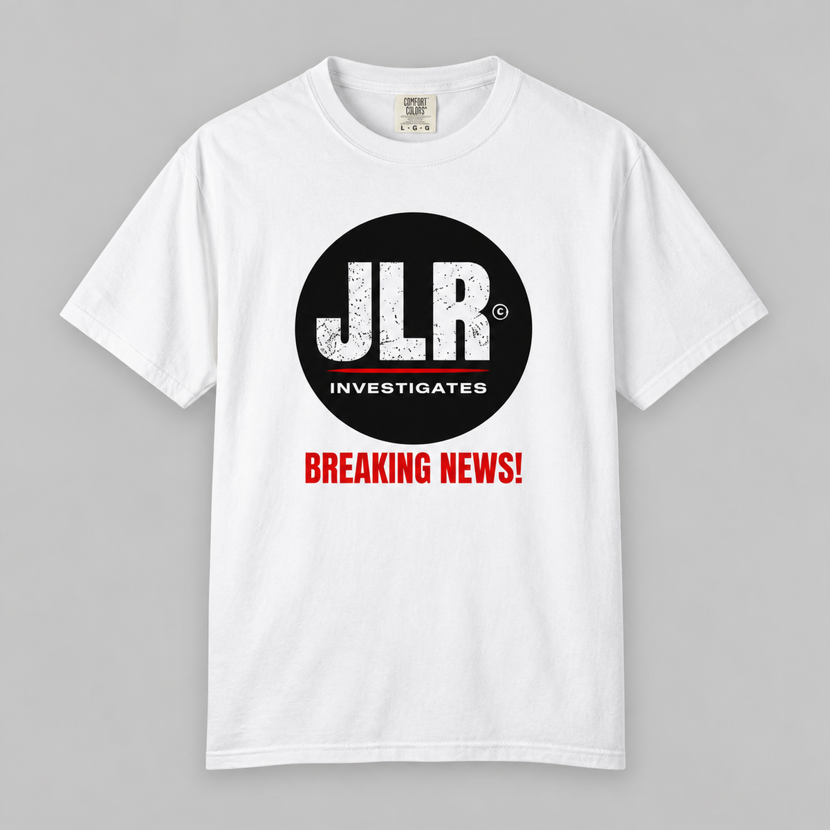 White T-shirt featuring the JLR© Investigates logo and red “BREAKING NEWS!” graphic, displayed front-facing on a light grey background
