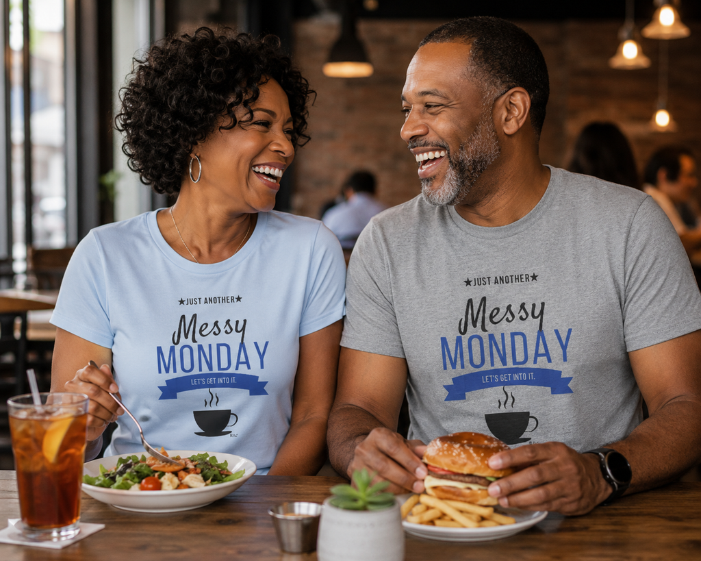 Two people wearing Messy Monday t-shirts sitting at a table with coffee and food